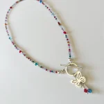 Detalle de collar colorido con cristales y mariposa artesanal